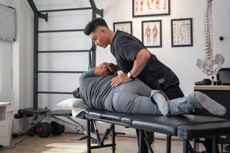 A person gently massaging a sore spot on their upper shoulder while seated in a cozy living room.