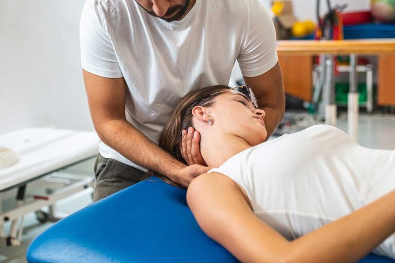 A clinician performing a gentle spinal adjustment on a patient lying face down in a bright clinic room.